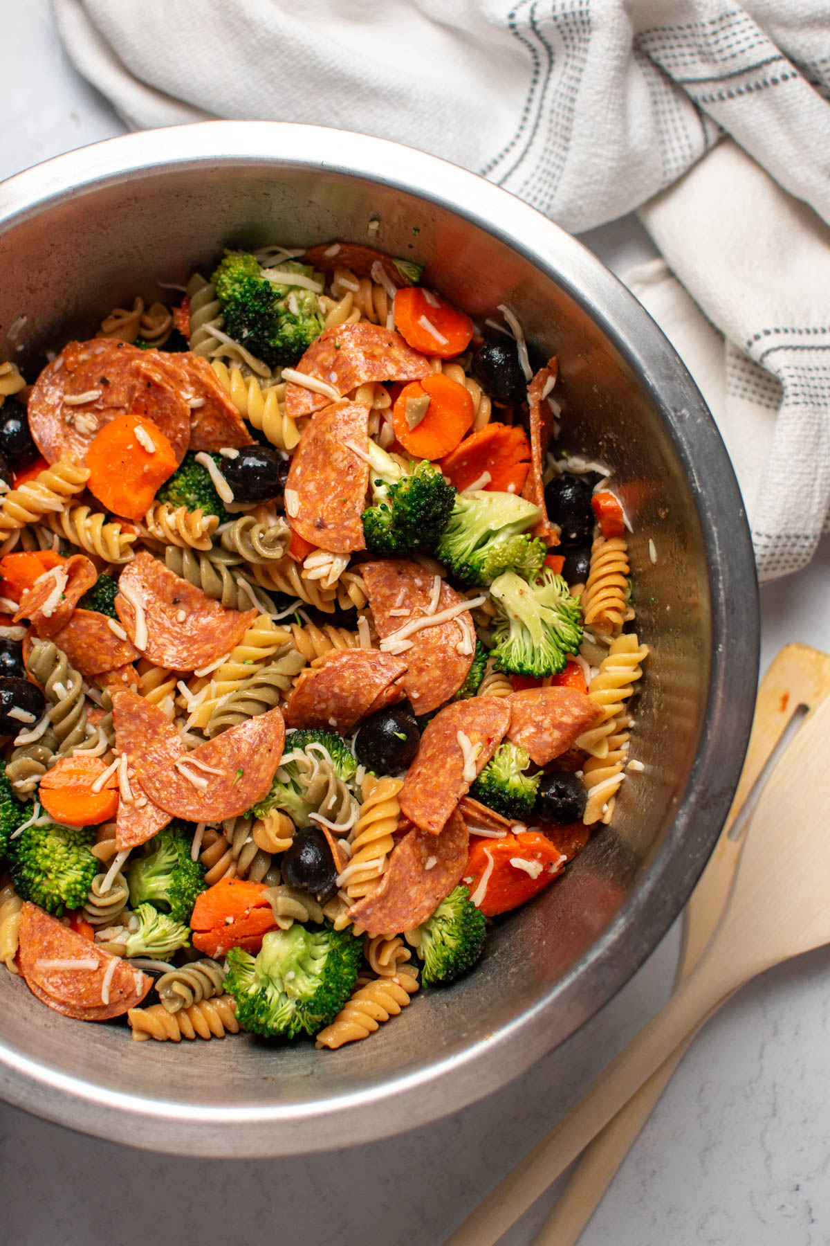 Tri color pasta salad with pepperoni and vegetables in large metal mixing bowl.
