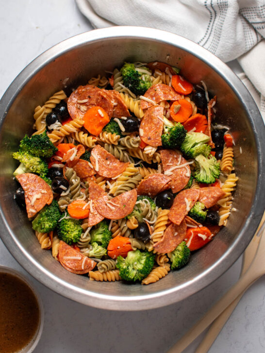 Metal bowl of tri color pasta salad with olives and pepperoni on marble table top.
