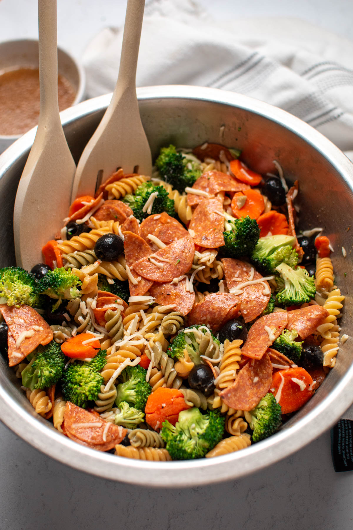 Two wooden spoons rest in bowl of Italian pasta salad with fresh vegetables.