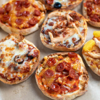 Several air fryer English muffin pizzas with pepperoni, barbeque sauce, and cheese on baking sheet.