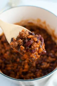 Wood spoon holding baked beans with ground beef and bacon.