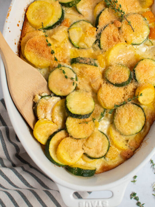 Zucchini and squash casserole in white baking dish with wood spoon and sprigs of thyme.