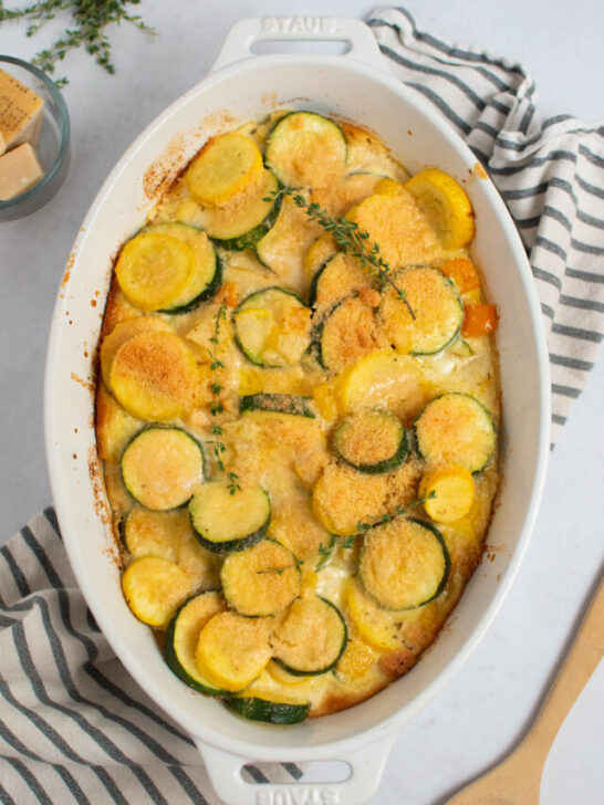 White baking dish with zucchini and yellow squash casserole topped with parmesan and thyme.