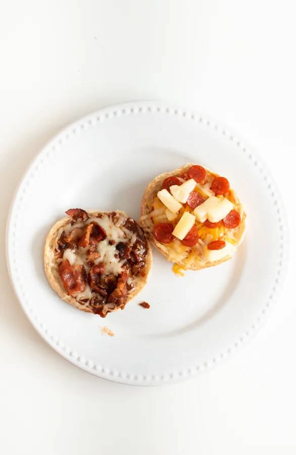 A BBQ bacon and a Hawaiian English muffin pizza on white dinner plate.