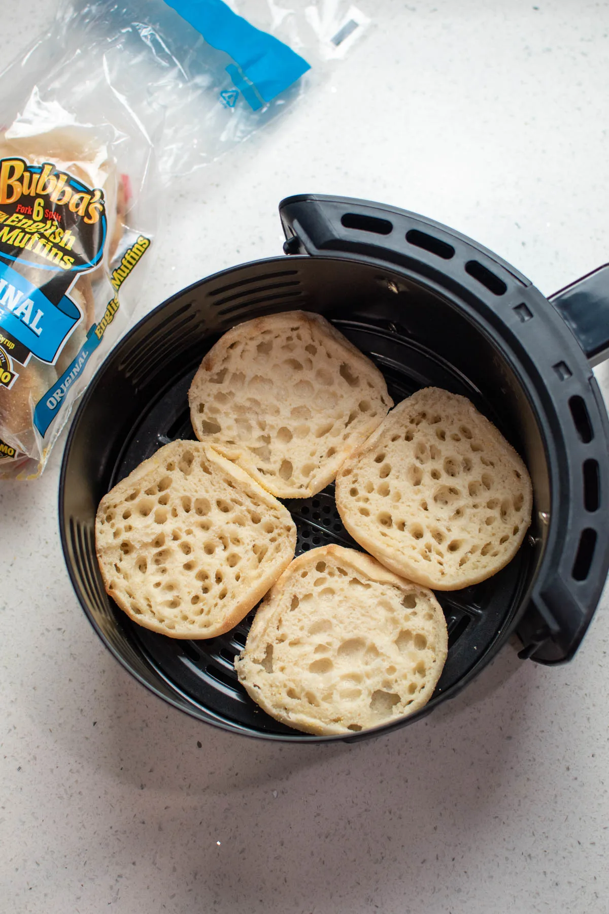 Four English muffin halves in air fryer on counter.
