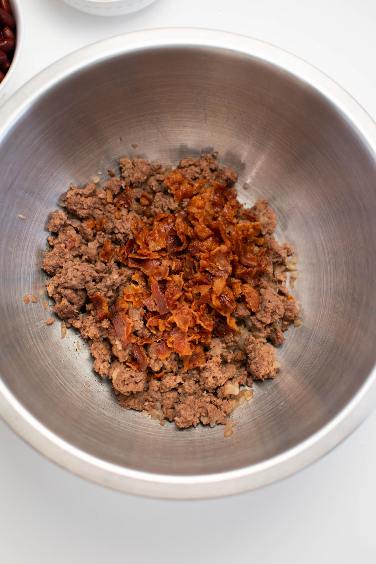 Ground beef and crumbled bacon in metal mixing bowl.