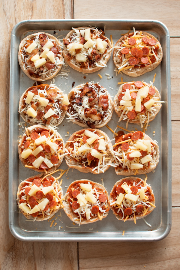 Several different kinds of kid-friendly English muffin pizzas on metal sheet pan.