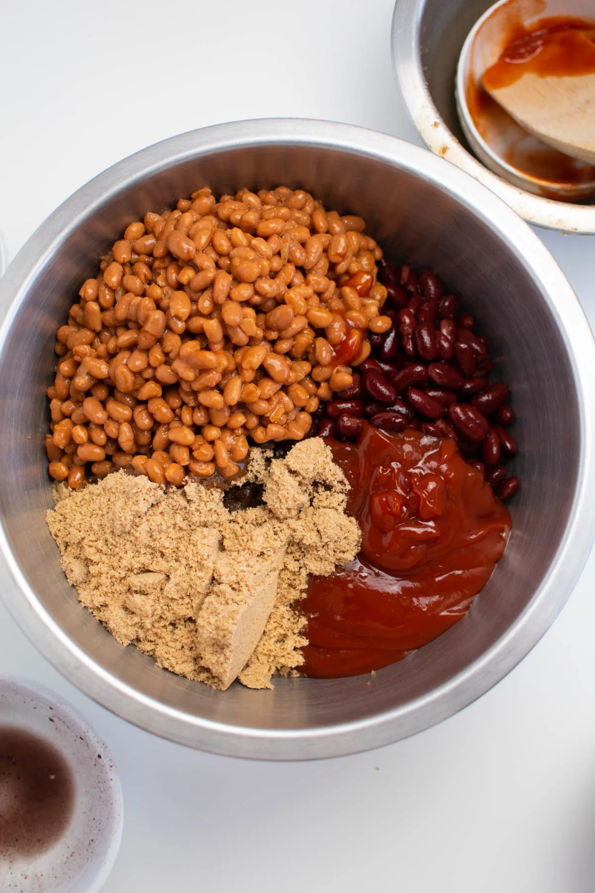 Pork and beans, ketchup, and brown sugar in metal bowl.