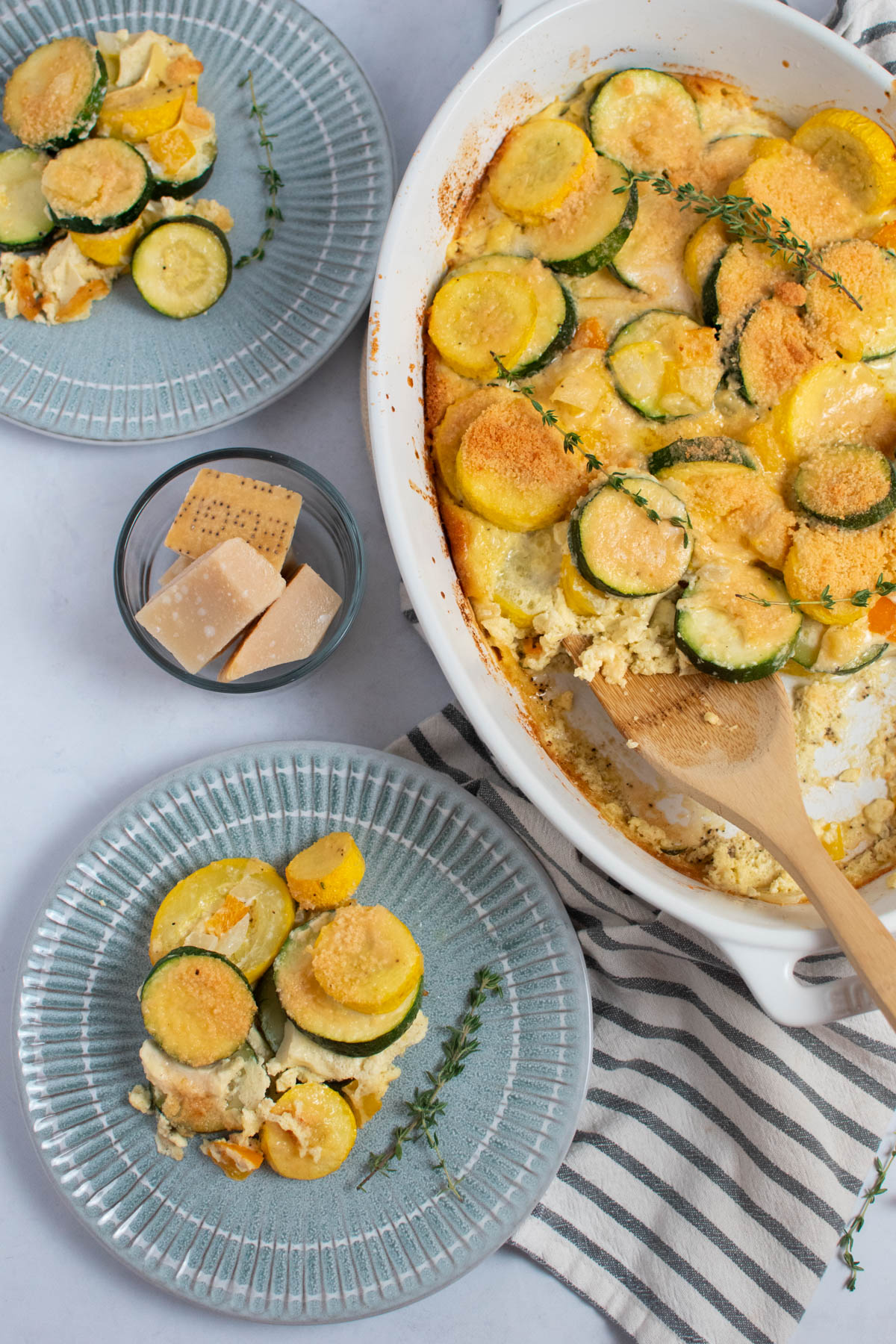 Two plates and white baking dish with posh squash topped with parmesan and thyme.