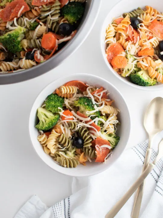 Tri color pasta salad recipe in white bowls next to large metal mixing bowl.