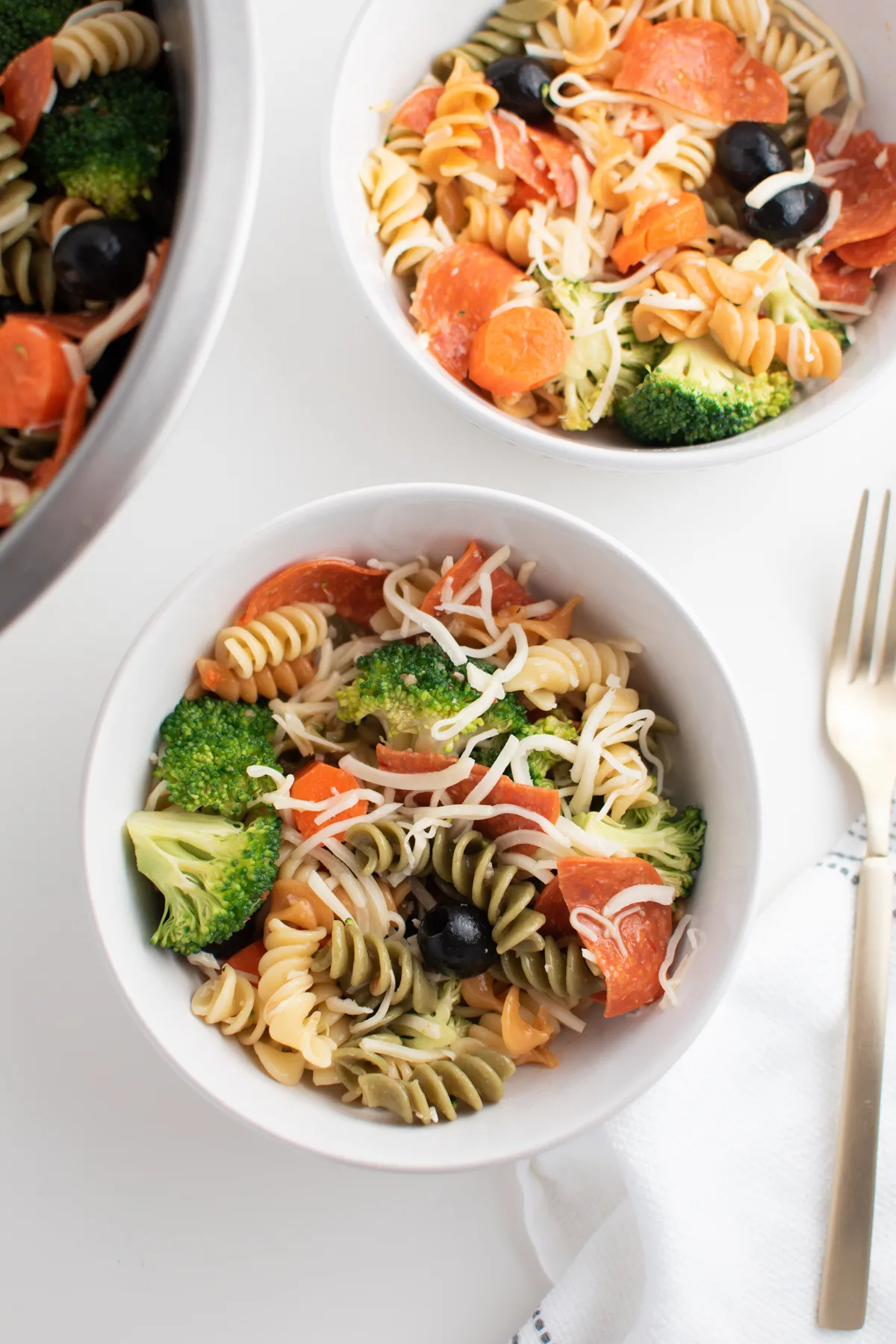 Tri color pasta salad with Italian dressing in white bowls with fork.