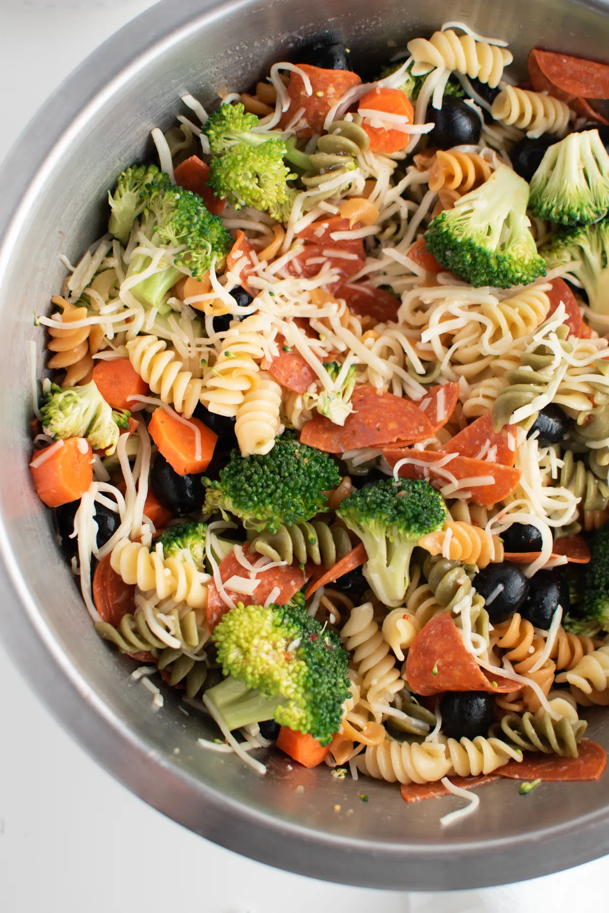 Close up of zesty Italian pasta salad in large metal mixing bowl.