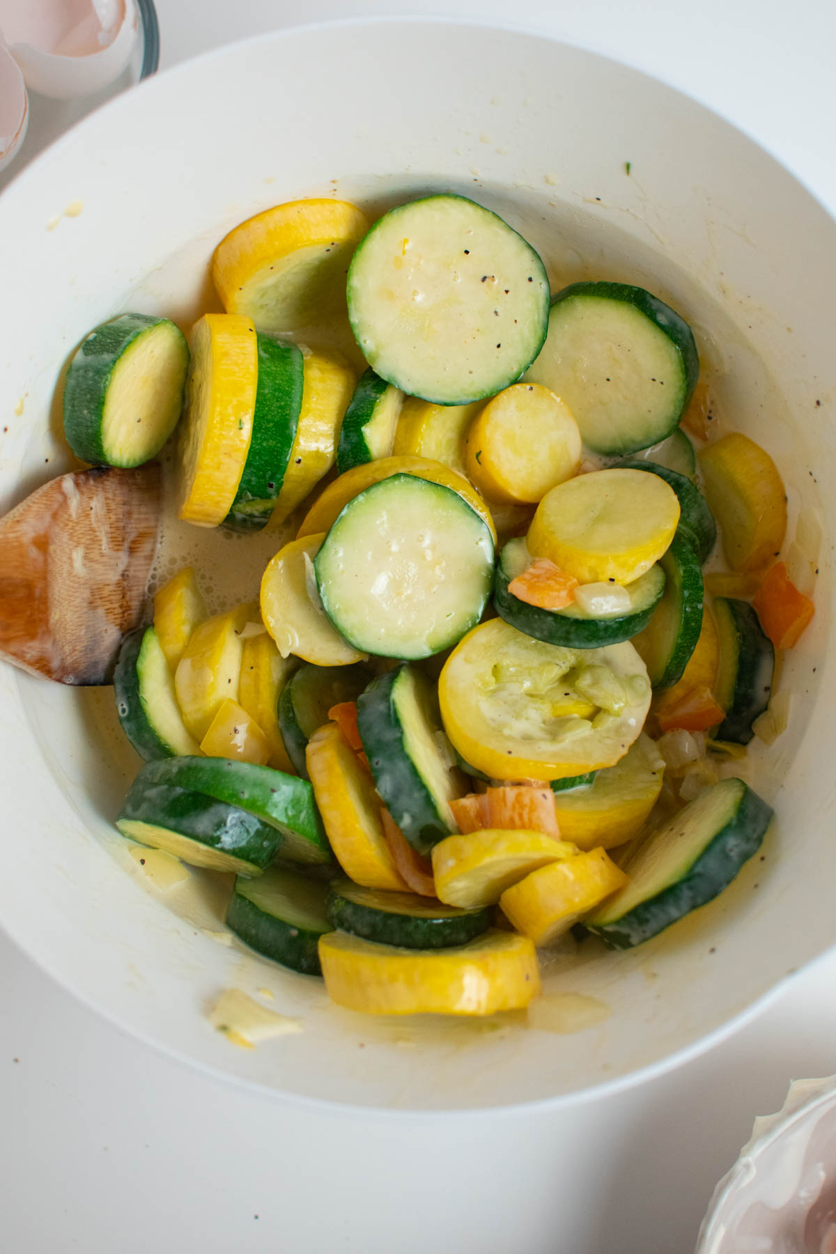 Zucchini and squash covered in egg mixture in white bowl.