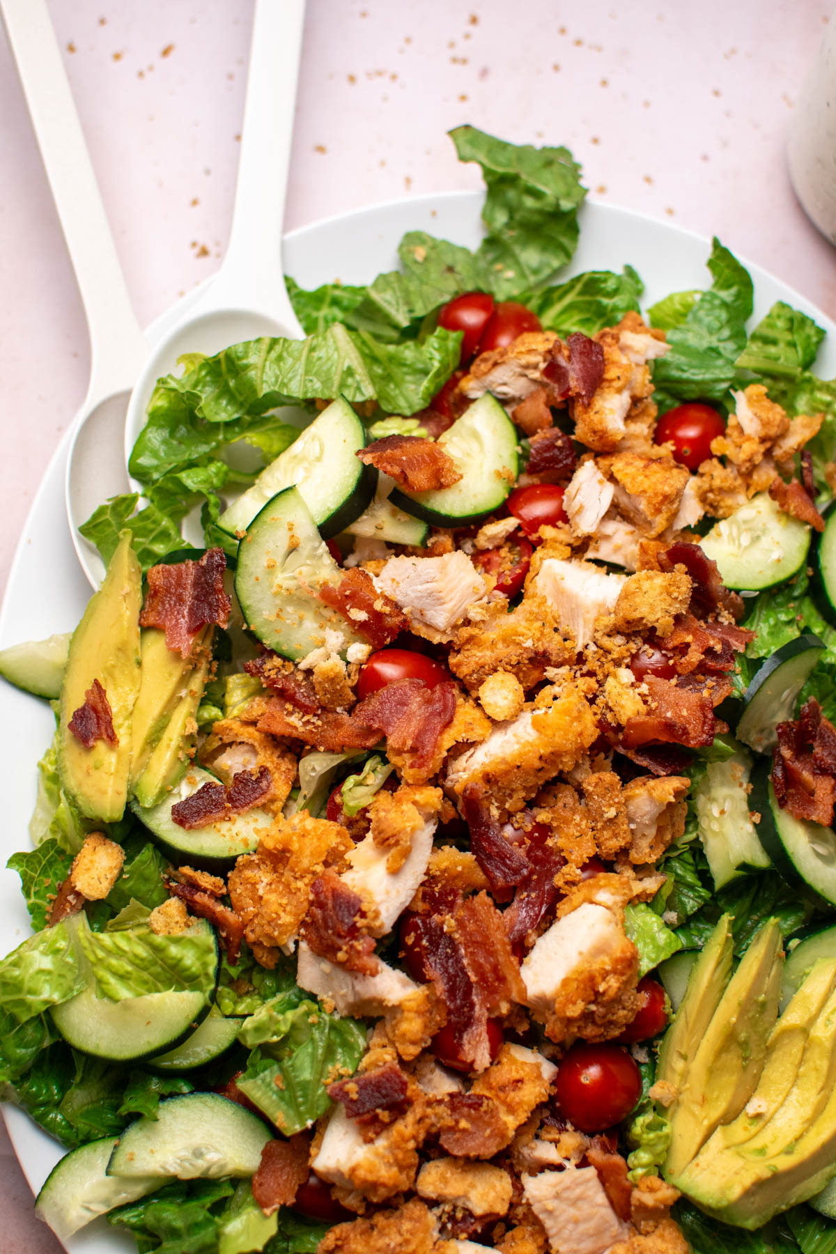 Two serving spoons in BLT salad with crispy chicken and avocado .