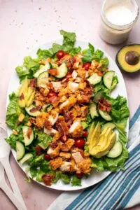 White platter of BLT salad with crispy chicken next to homemade ranch and avocado half.