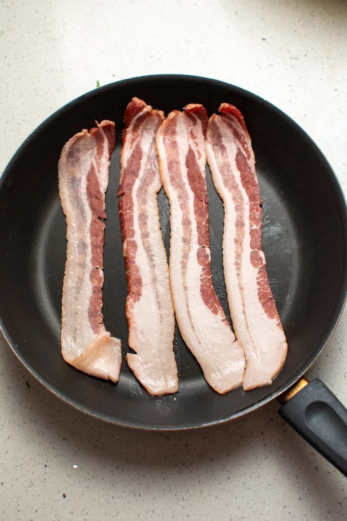 Four pieces of raw bacon in black frying pan.
