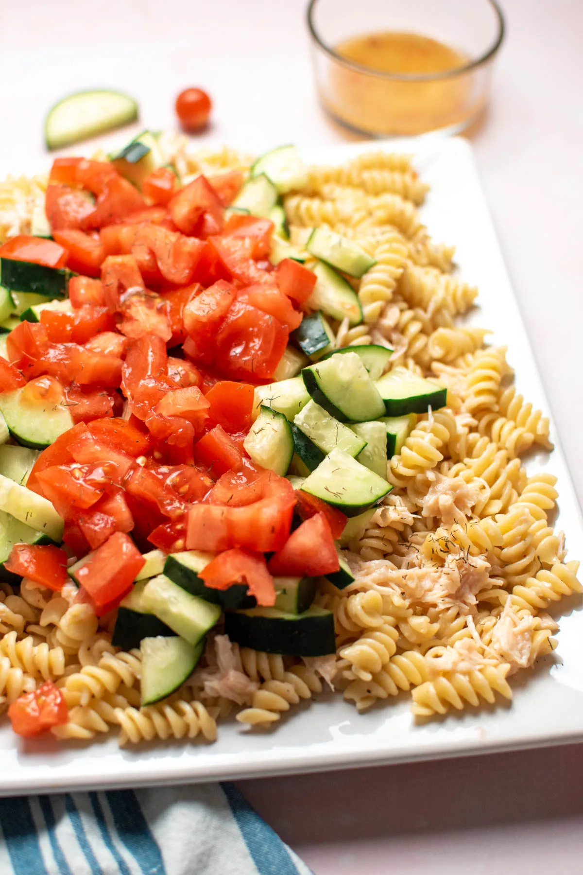 Chicken pasta salad with rotini, tomatoes, and cucumbers, on large square platter.