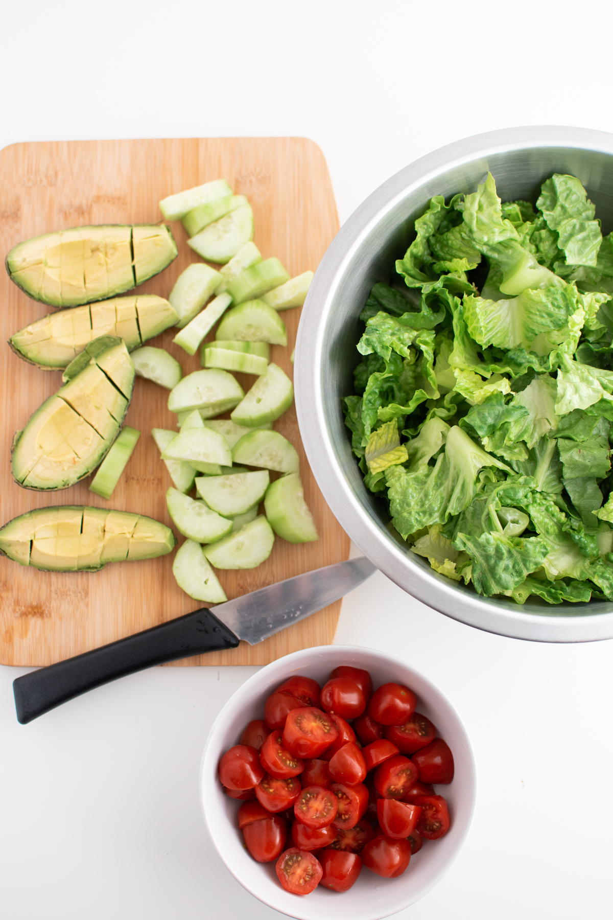 Chopped salad ingredients on white table, including lettuce, tomato and avocado.