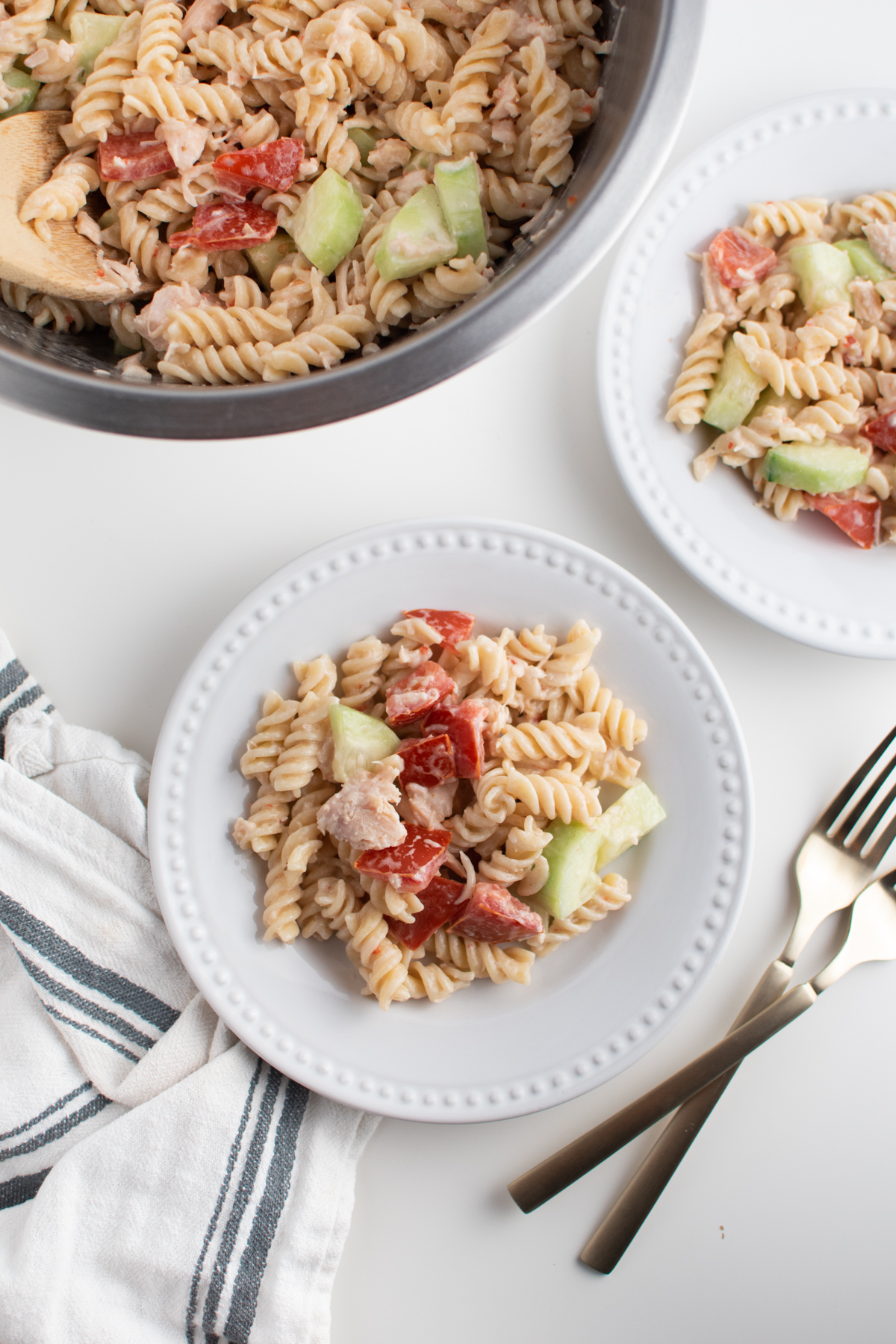 Pasta salad with rotini on white plates next to salad bowl and utensils.