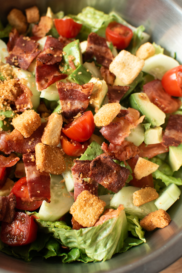 Recipe for BLT salad in large metal mixing bowl with avocado and croutons.