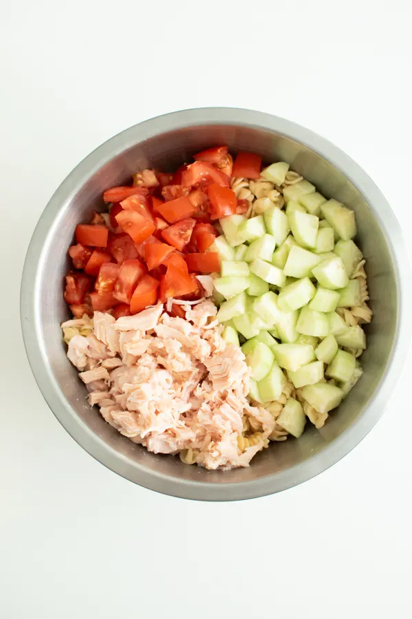 Rotini pasta salad recipe in a mixing bowl with cucumbers and tomatoes.