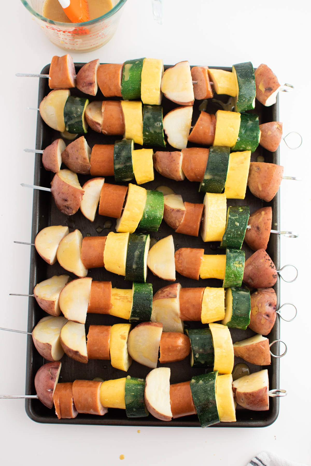 Eight sausage and potato kabobs on metal baking sheet covered in honey glaze.
