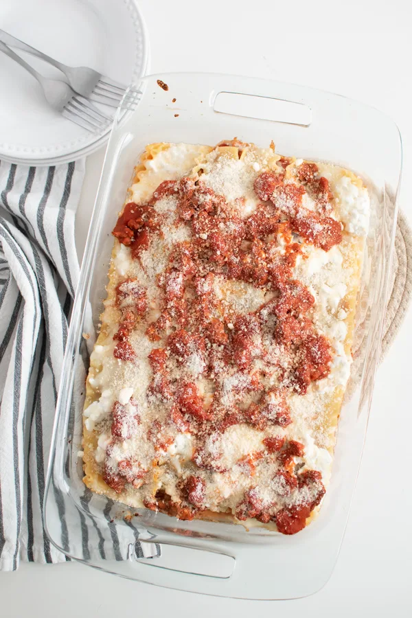 Baking dish of lasagna with cottage cheese on white dinner table.