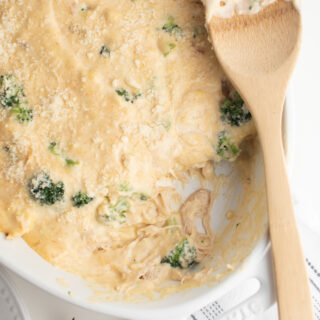 Chicken broccoli casserole recipe in a casserole dish with wood spoon and kitchen towel.