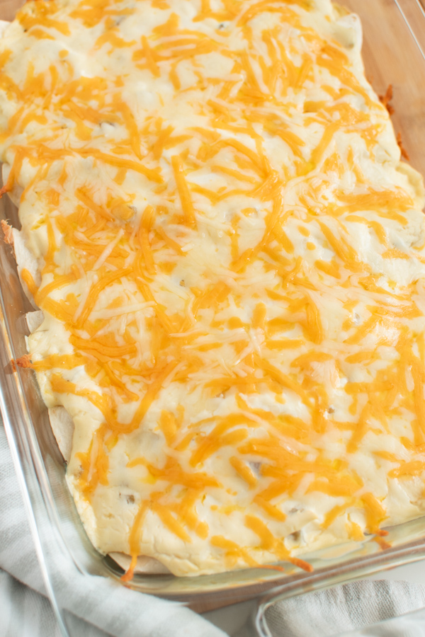 Close up of sour cream enchiladas with melted cheese in clear glass baking dish.