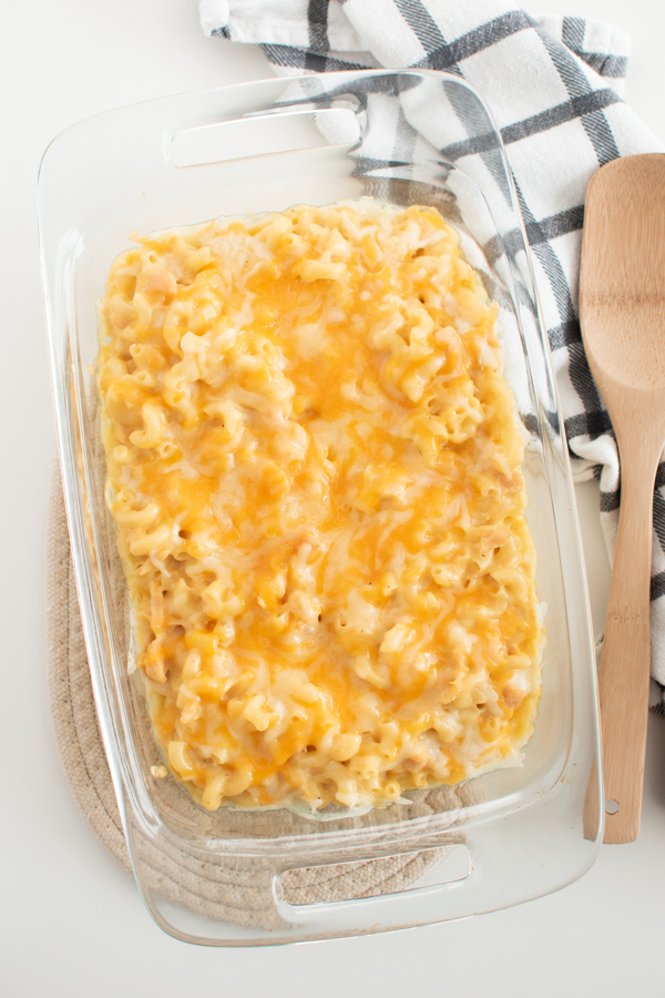 Macaroni casserole in clear glass baking dish with wooden spoon and kitchen towel.
