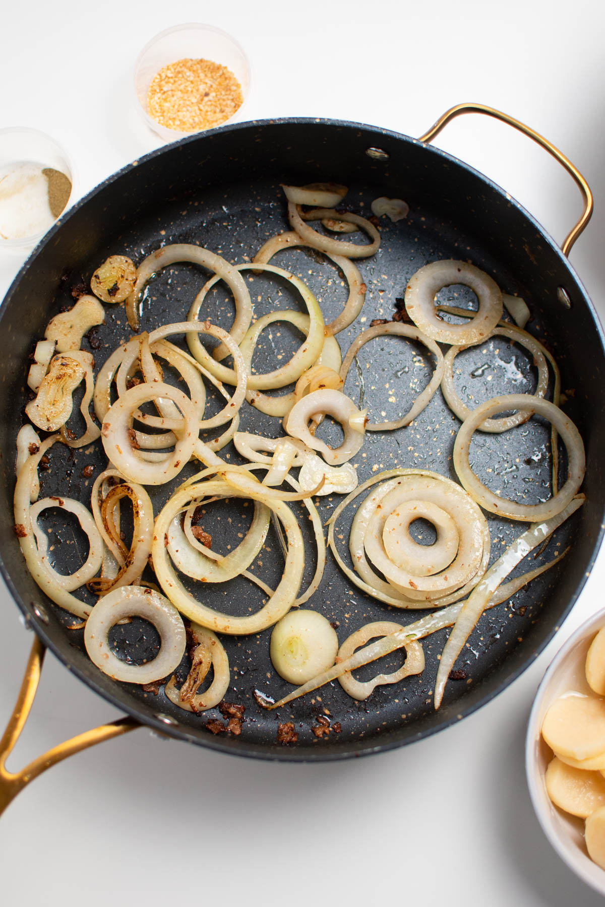 Several cooked onion slices in large black skillet, all on white table.