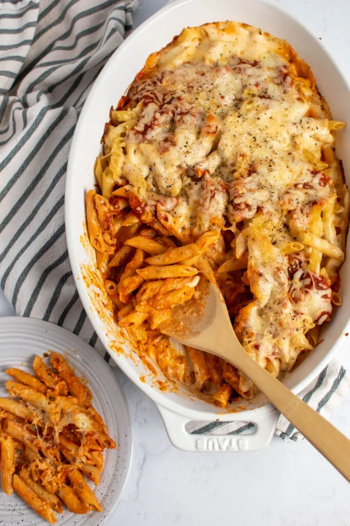 Wood spoon in baking dish full of creamy pasta bake topped with mozzarella cheese.