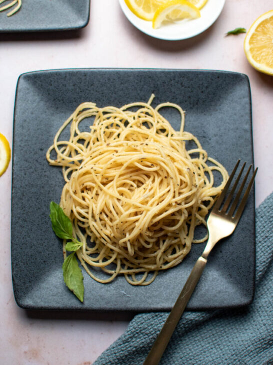 Gray square plate with pile of lemon basil pasta, fresh basil leaves, and gold fork.