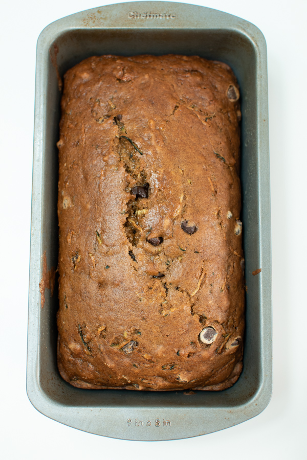 Pumpkin zucchini bread fresh out of oven in metal loaf pan on white surface.