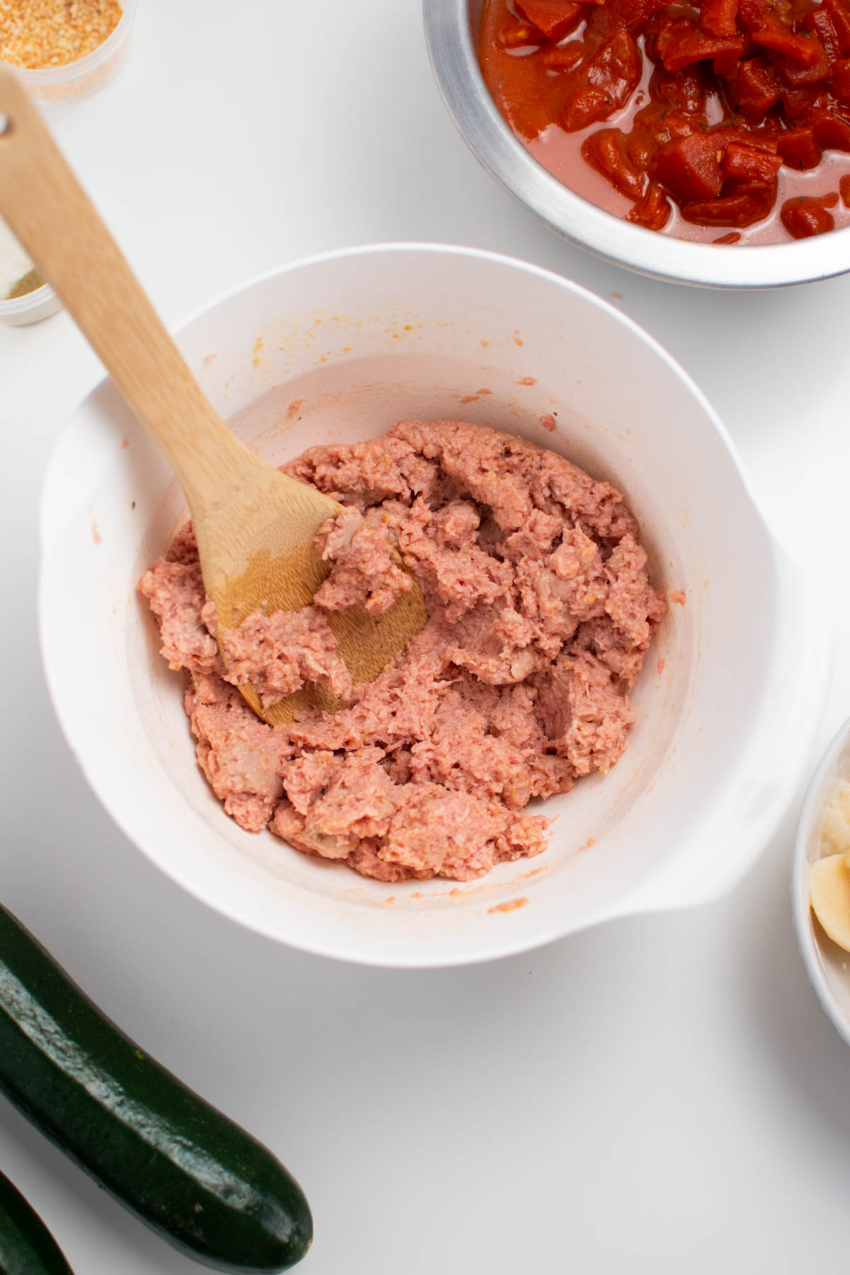Raw ground turkey in white bowl with wooden spoon.