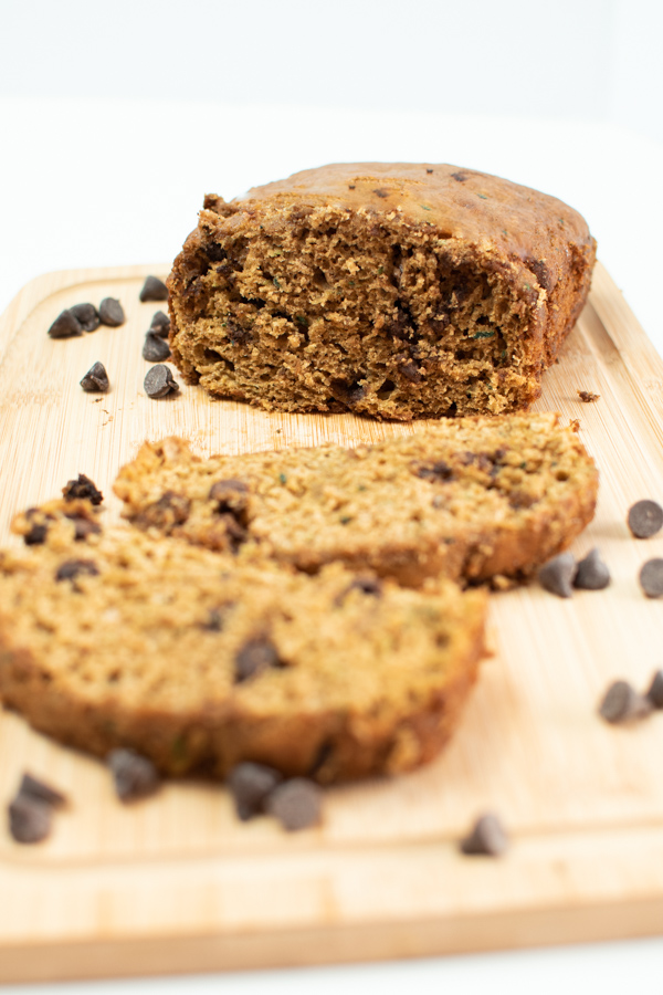 Slices of healthy pumpkin zucchini bread on wooden cutting board surrounded by chocolate chips.