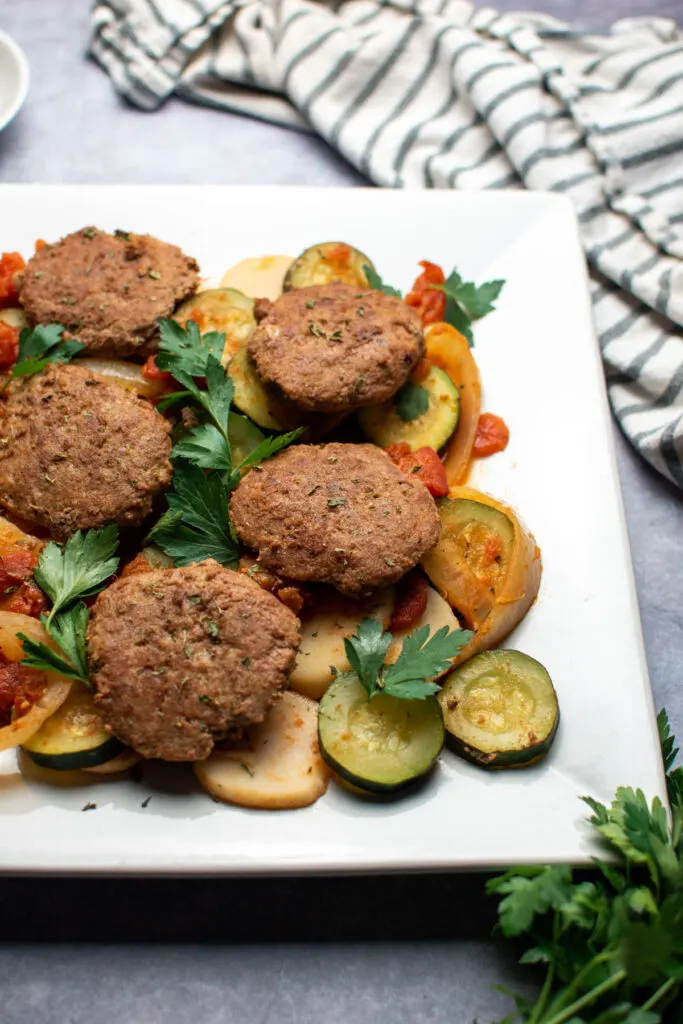 Italian ground turkey patties with vegtables provencal on large white platter, kitchen towel nearby.