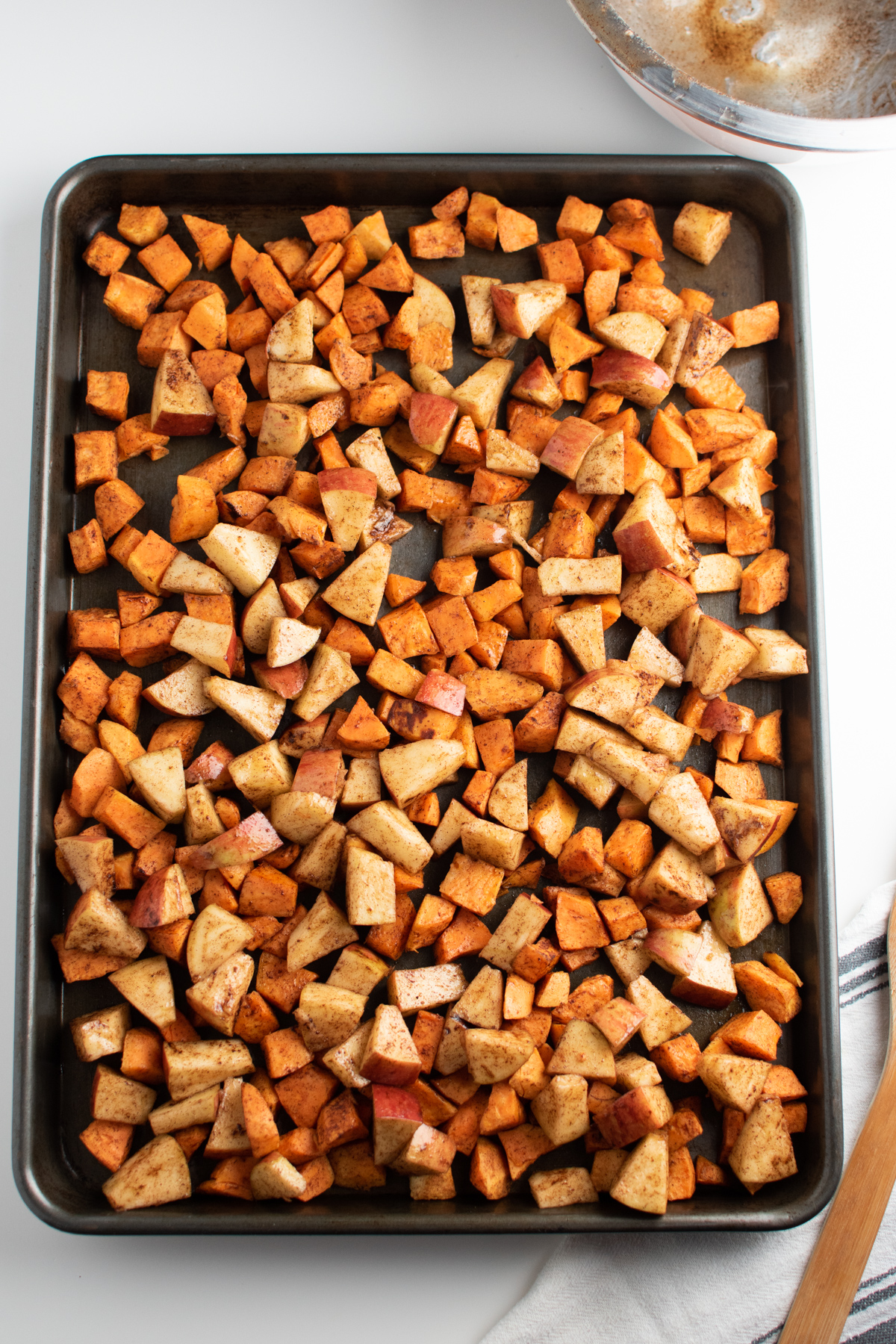 Roasted sweet potato and apple cubes cover a metal sheet pan.