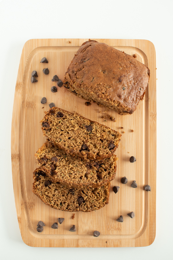 Pumpkin zucchini bread and slices on a cutting board with scattered chocolate chips.