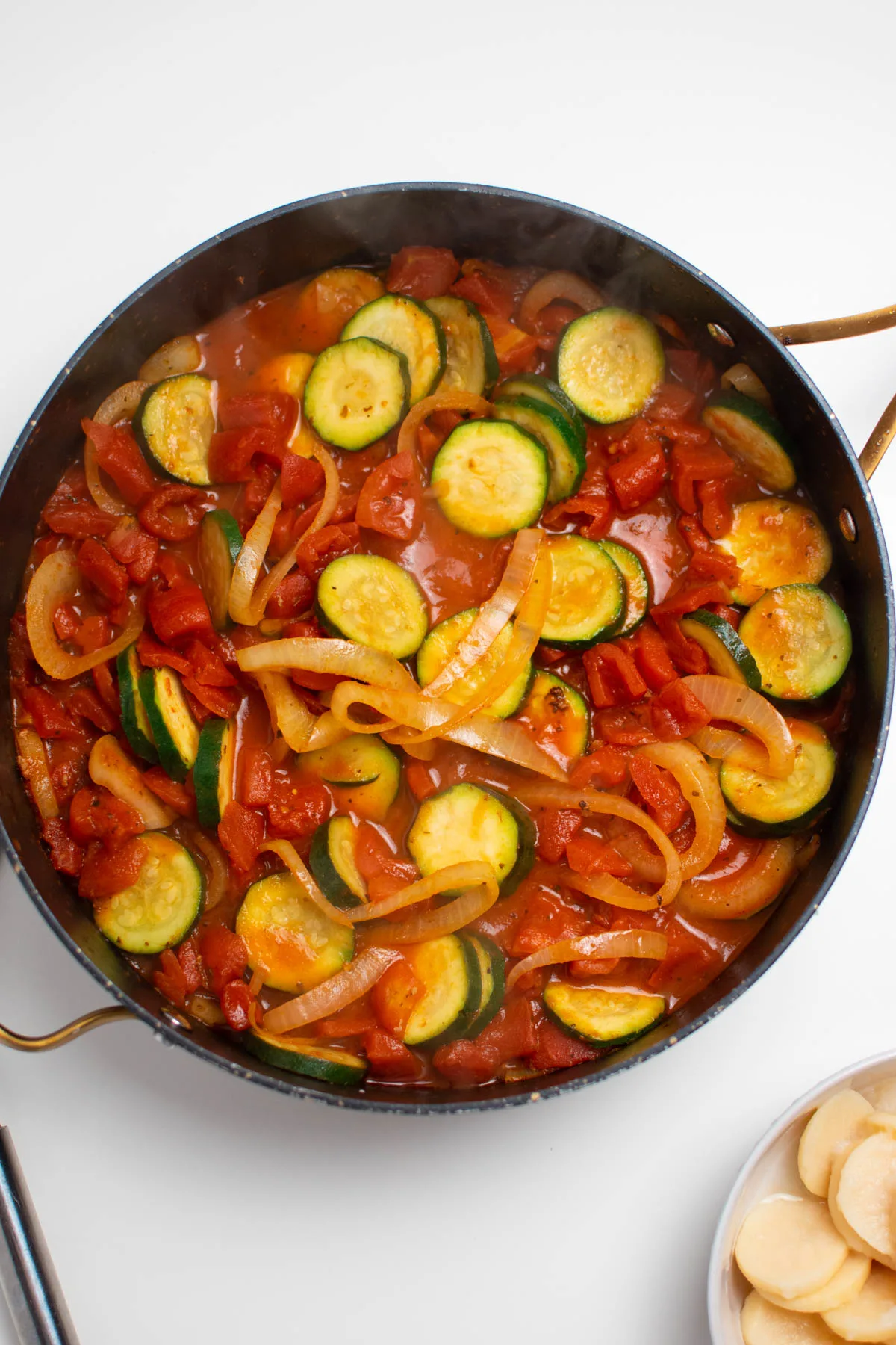 Black skillet full of sauteed vegetables including zucchini, onion, and tomatoes.
