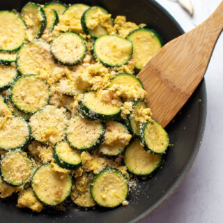 Zucchini and eggs with parmesan cheese in black frying pan with wood spoon.