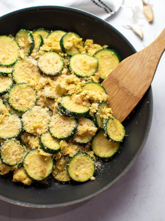 Zucchini and eggs with parmesan cheese in black frying pan with wood spoon.