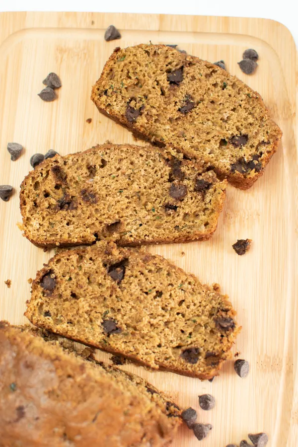 Several slices of zucchini bread with chocolate chips on wooden cutting board.