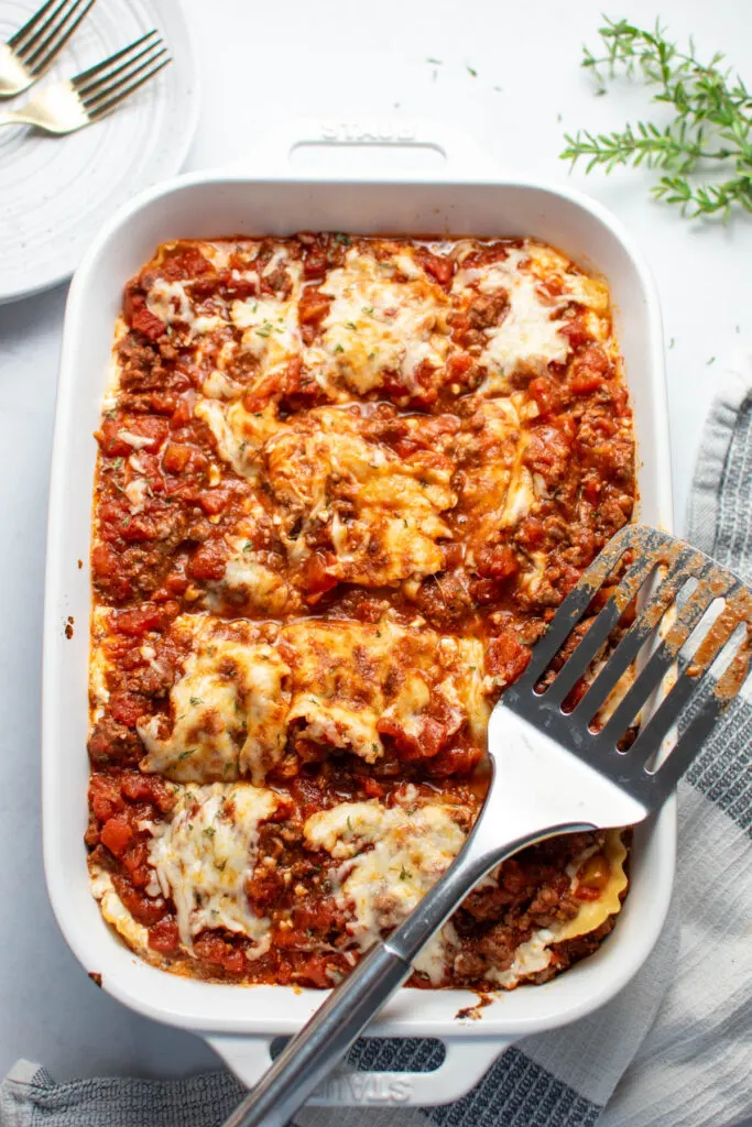 Large white baking dish with cut pieces of lasagna with cottage cheese and spatula on top.