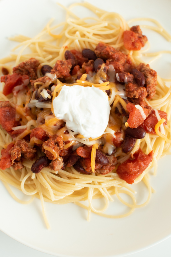 Close up of Cincinnati chili recipe topped with sour cream on white plate.