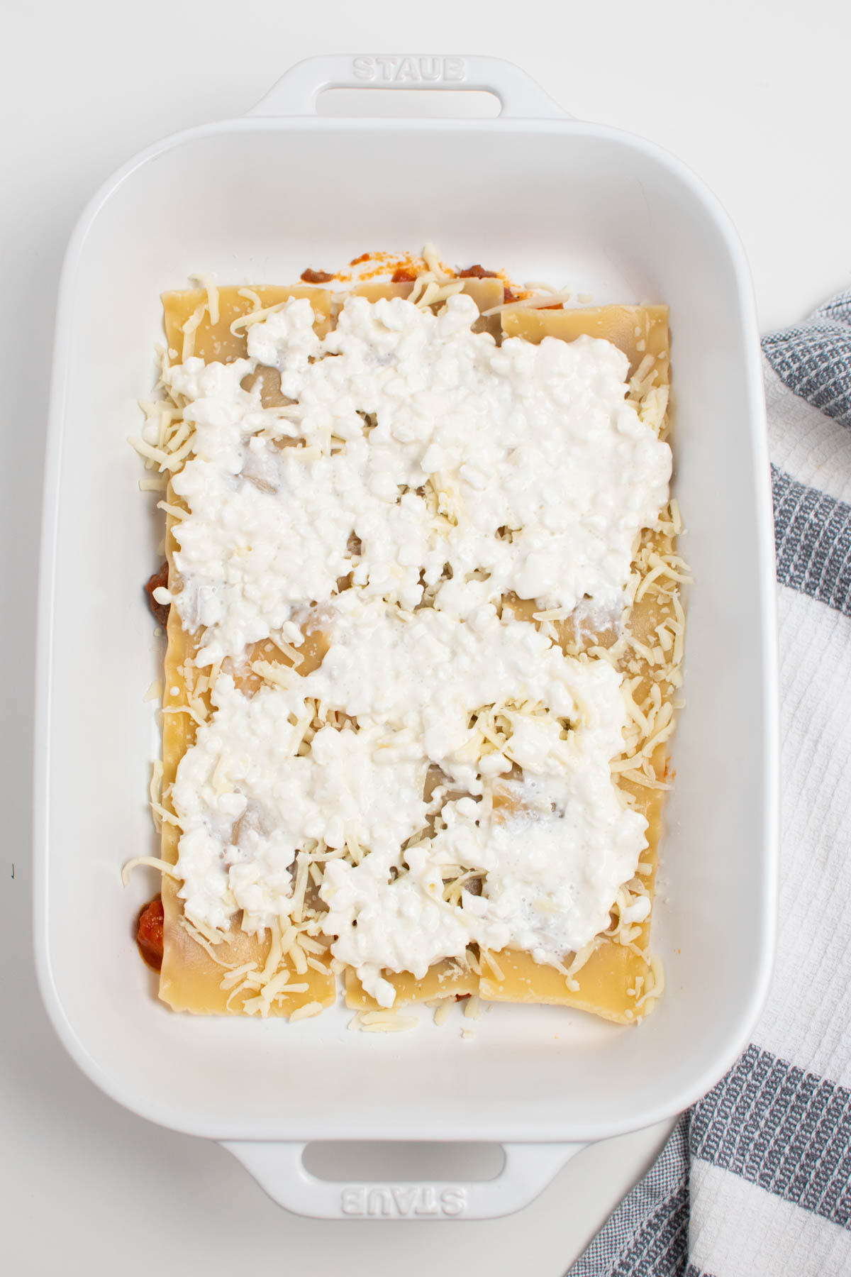 Spoonfuls of cottage cheese and shredded mozzarella on lasagna noodles in baking dish.