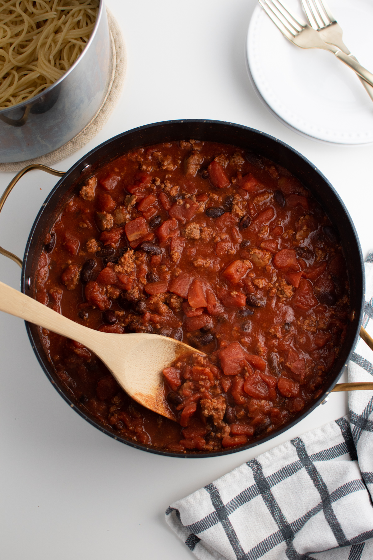 Pan of Cincinnati chili with wooden spatula next to pot of spaghetti.