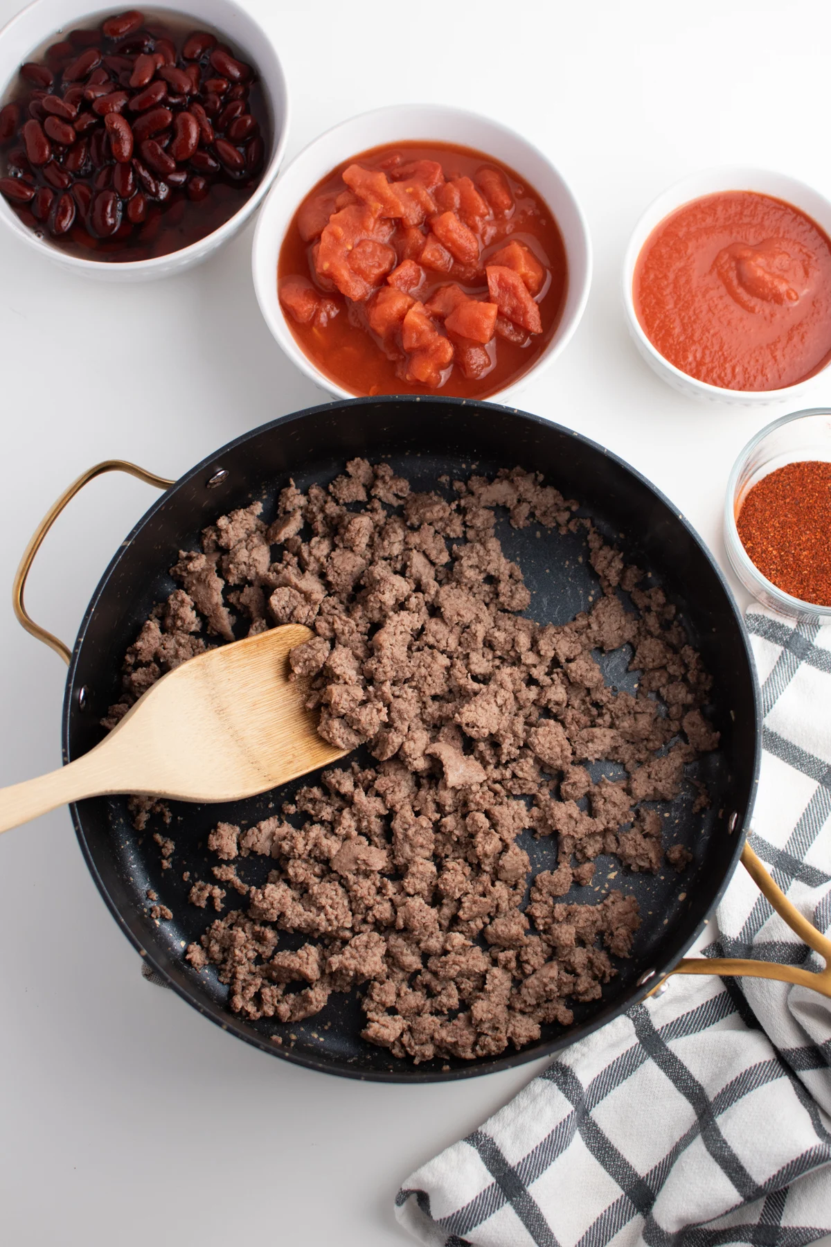 Black skillet filled with cooked ground beef next to kitchen prep bowls.