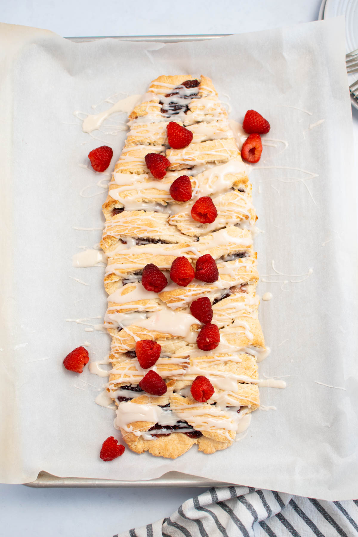 Raspberry filled pastry with fresh raspberries on parchment paper and baking sheet.