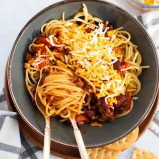 Fork and spoon twirled around some spaghetti with chili all in green bowl.